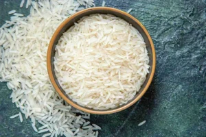 Riz blanc cru dans un bol vu de dessus, grains éparpillés sur une surface foncée.