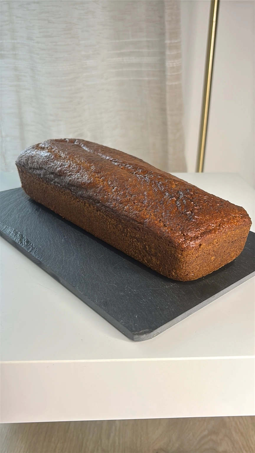 Pain d’épices sain et moelleux NutriQore posé sur une planche en ardoise, avec une croûte dorée et brillante, photographié en lumière naturelle
